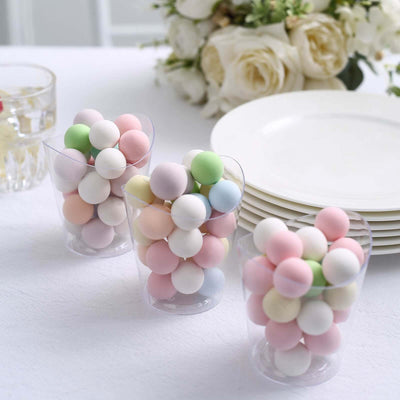 Colorful pastel candy balls in clear cups on a table with plates and flowers.