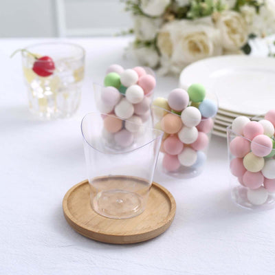 Clear plastic dessert cup on bamboo coaster with colorful candies.