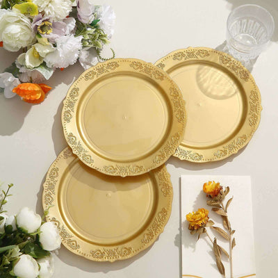 Three elegant gold decorative plates on a white table with flowers.