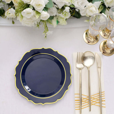 Navy blue decorative plate with gold trim, set beside cutlery and floral arrangement.