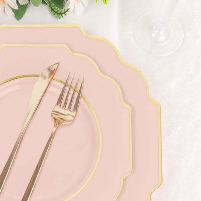 Pink scalloped dinner plates with gold trim and cutlery on a white tablecloth.