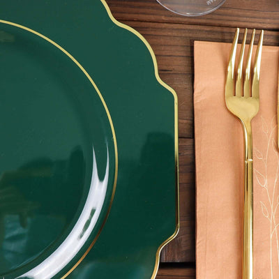 Green scalloped plate with gold trim and elegant gold fork on a brown napkin.