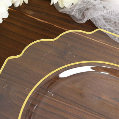Clear glass plate with scalloped edge and gold trim on wooden surface.