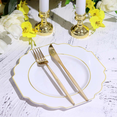 Elegant white plate with gold trim, fork, and knife on a floral table setting.