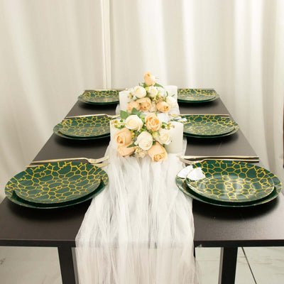 Elegant green and gold patterned dinner plates on a styled dining table with flowers.