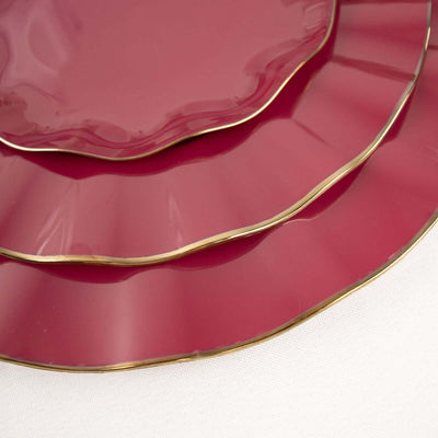 Stacked burgundy plates with gold trim on a white background.