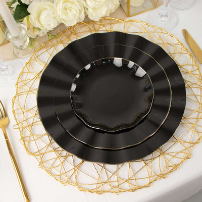 Elegant black dinnerware set layered on a gold charger with floral decor in background.