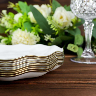 Elegant white plates with gold trim stacked beside floral arrangement and crystal glass.