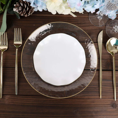 Elegant white plate on a gold rimmed charger with forks and knife on a wooden table.
