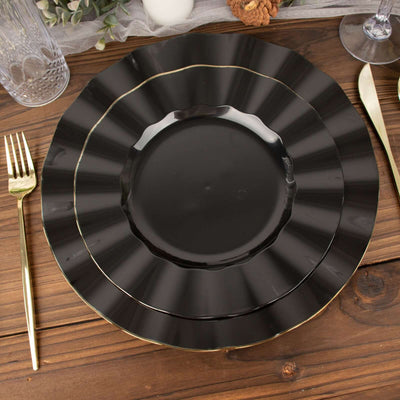 Black scalloped dinner plate with gold rim on a wooden table setting.