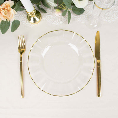 Clear plate with gold rim, fork, and knife on a beautifully set table.