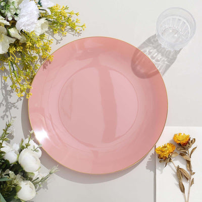Pink plate with gold rim on a table with flowers and glass.