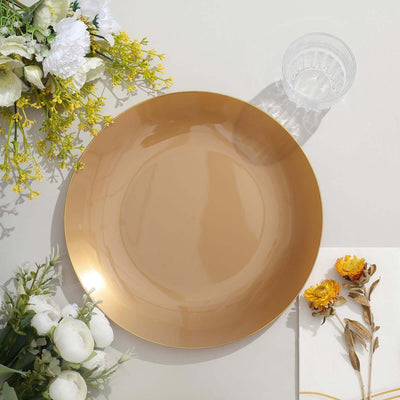 Gold decorative plate on a neutral surface with flowers and a glass.