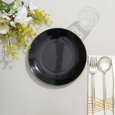 Elegant black dinner plate with gold rim, styled with cutlery and floral accents.