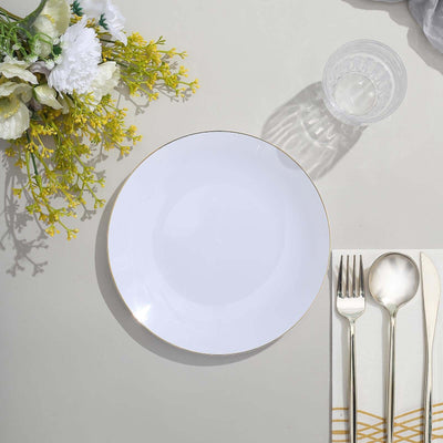 Elegant white plate with gold rim set on a table with utensils and floral decor.