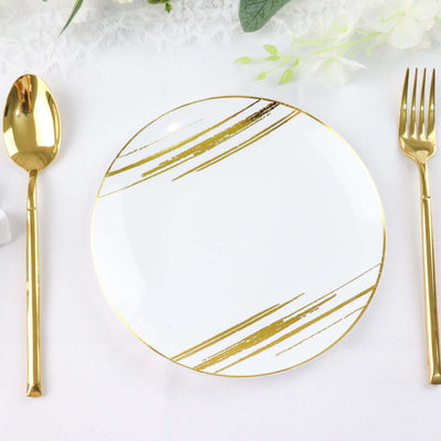 Elegant white plate with gold brushstroke design, surrounded by golden utensils.