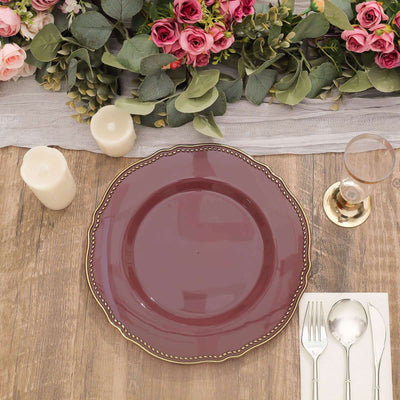 Elegant burgundy dinner plate with gold rim on a rustic wooden table setting.