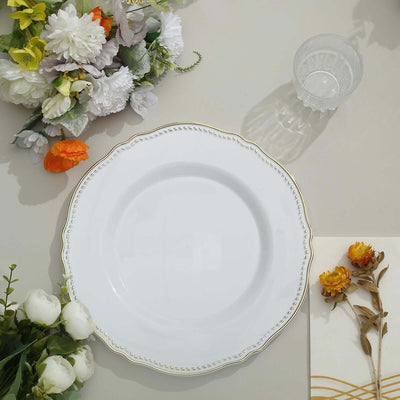 Elegant white plate with gold trim surrounded by flowers and a glass.