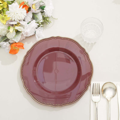 Burgundy decorative plate with scalloped edge and gold trim on a table setting.