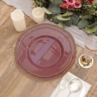 Elegant burgundy plate with gold rim on a wooden table setting.