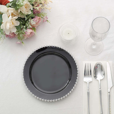 Elegant black plate with beaded edge, set for dining with cutlery and floral decor.