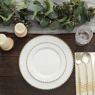 Elegant white dinner plates with gold bead accents on a rustic wooden table setting.