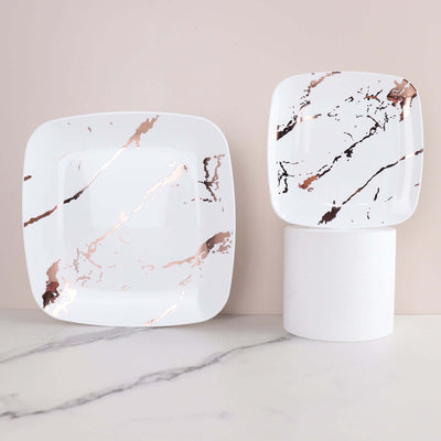 Rose gold marbled square plates on a marble surface.
