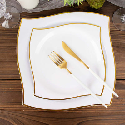 Elegant white plates with gold trim and cutlery on a wooden table.
