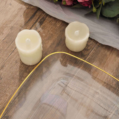 Clear glass platter with gold rim and two white candles on a wooden surface.