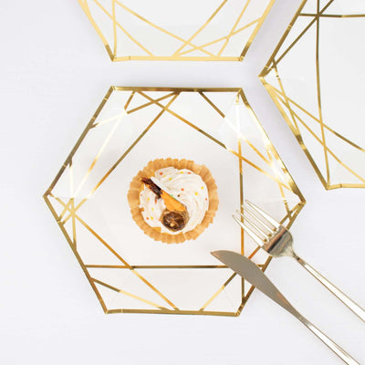 Geometric gold-accented plates with a cupcake and cutlery on a white background