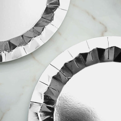 Silver disposable plates with scalloped edges on a marble surface.