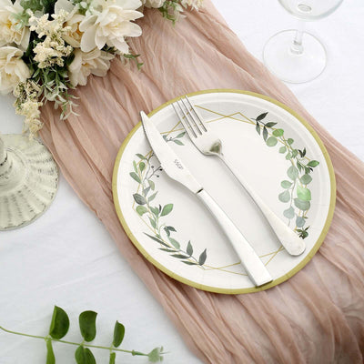 Elegant table setting with floral plate, silver cutlery, and soft fabric backdrop.