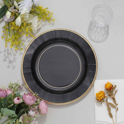 Elegant black plate with gold rim on a table with flowers and glass.