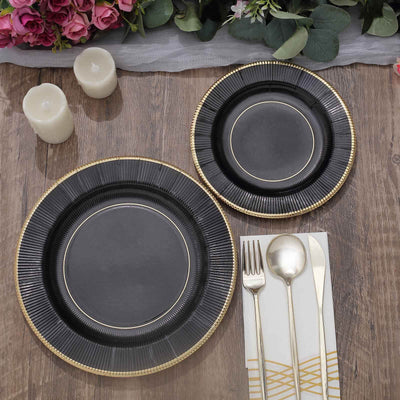Elegant black plates with gold rim on a wooden table with candles and floral accents.
