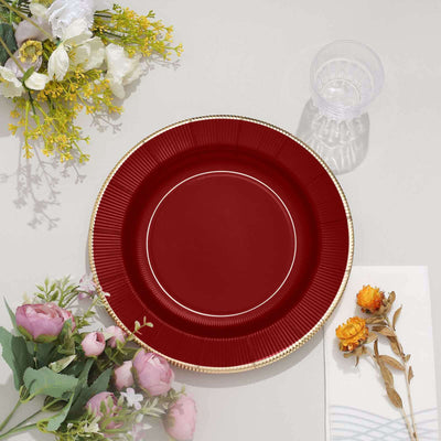 Elegant red plate with gold rim, surrounded by flowers and glassware.