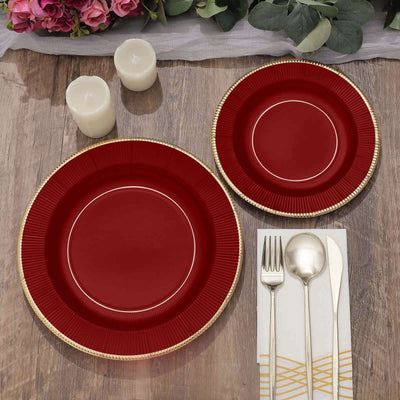 Elegant red and gold dinner plates set with cutlery on a rustic wooden table.