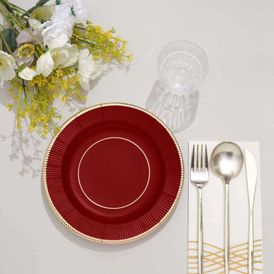 Red plate with gold rim, silver cutlery, and clear glass on a table setting.