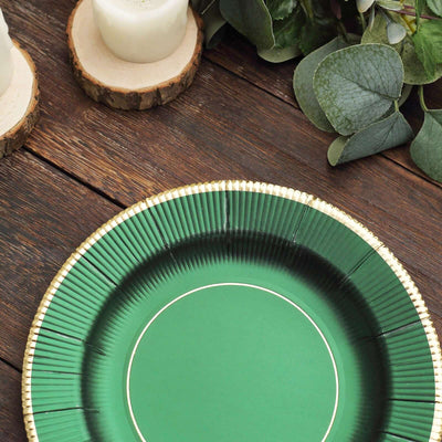 Green paper plate with gold rim on a wooden table surrounded by greenery.