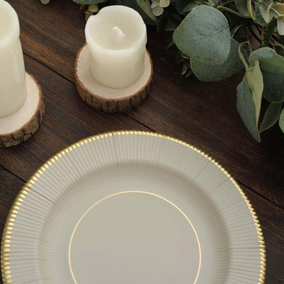 Elegant round plate with gold rim on rustic wooden table with candles and greenery.