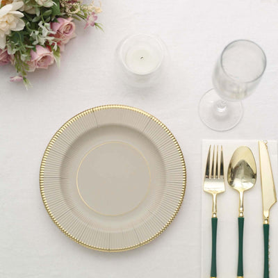Elegant dinner plate with gold rim, cutlery, and glassware on a table setting.
