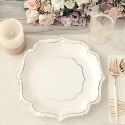 Elegant white scalloped plate with silver trim on a table setting.