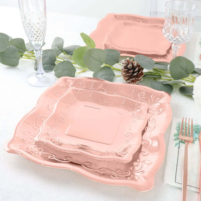 Pink decorative plates arranged on a table with greenery and glassware.