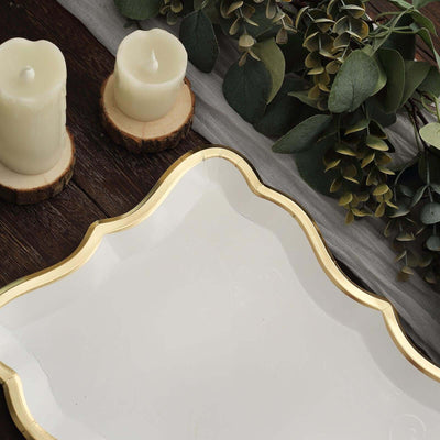 Elegant gold-trimmed serving tray with candles and greenery on a rustic wooden surface.