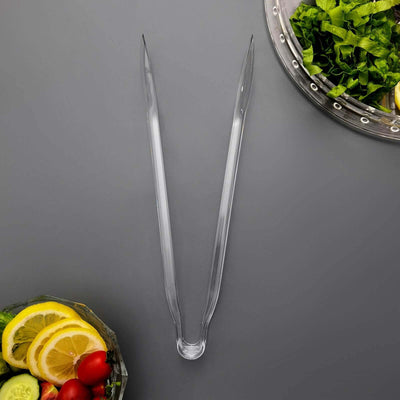 Clear plastic tongs on a gray background with fresh vegetables.
