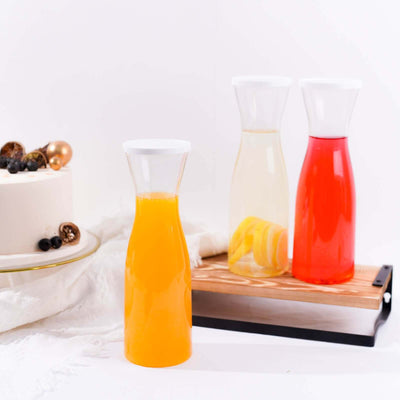 Colorful glass carafes with drinks on wooden tray and cake in the background.