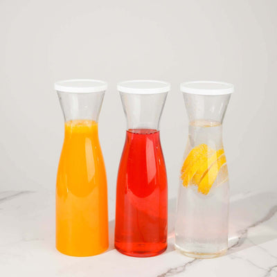 Three glass carafes with orange juice, red beverage, and lemon water on a marble surface.