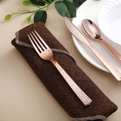 Rose gold fork on a brown napkin with plate and cutlery in the background.