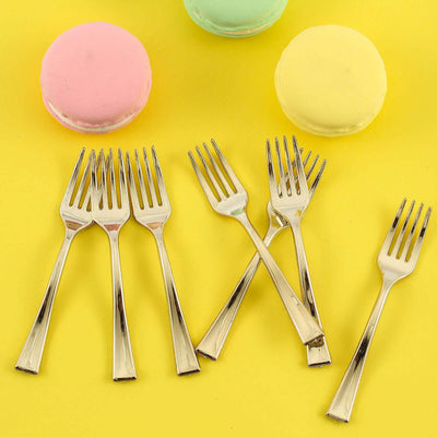 Set of six silver dessert forks next to colorful macarons on a yellow background.