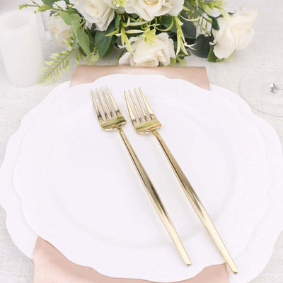Elegant gold forks on a white plate with floral arrangement in the background.