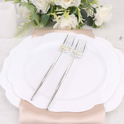 Elegant white dinner plate with silver forks, styled with flowers and fabric.